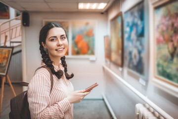 Portrait of smiling caucasian woman holding a smartphone. Excursion with audio guide in the art gallery. Exhibition and visit to the museum