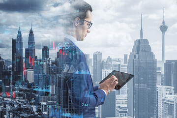 Canvas Print - Attractive young european business man using tablet with creative growing financial forex chart graph on blurry city background. Market, stock and trading concept. Double exposure.