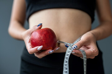 Trainer holding green apple and measuring tape for measuring body in fashionable sportswear