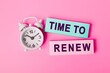 © Red Cristal - White alarm clock isolated on vivid pink background with text TIME TO RENEW, written on paper notes. Closeup of a personal agenda, top view. Motivational quote