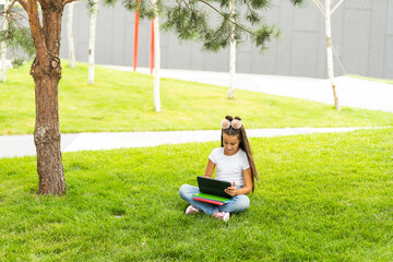 Wall Mural - Little girl sitting on grass and playing tablet pc