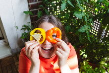 Happy Teenage Girl Looking Through Yellow Bell Pepper Slices On Balcony