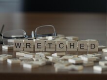 Wretched Word Or Concept Represented By Wooden Letter Tiles On A Wooden Table With Glasses And A Book