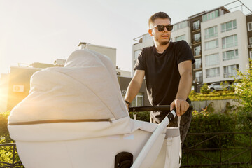 Portrait of a young father while walking with a child in a stroller. A man walks with a baby in a stroller around the city.