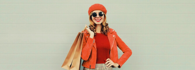 Autumn portrait of beautiful happy smiling young woman with shopping bags wearing red jacket, beret on gray background