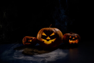 Wall Mural - Pumpkins with carved grimaces and candles inside in the dark for halloween. Jack o latern in smoke.