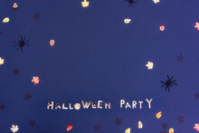 Halloween Party Phrase Lettering Made Of Golden Letters On The Dark Purple Blue Background With Autumn Leaves, Black Stars Sequins And Spiders With Copy Space For Text. Selective Focus.