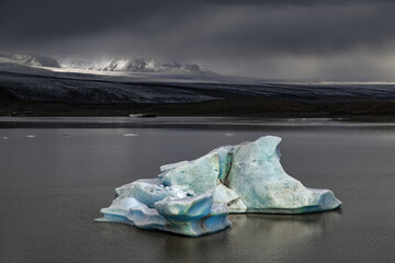 Wall Mural - fjallsarlon glacier lagoon, iceland, on a stormy day. a blue iceberg floats in the lagoon and sunlig