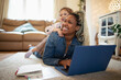 © Caia Image - Daughter laying on happy mother working at laptop on floor at home