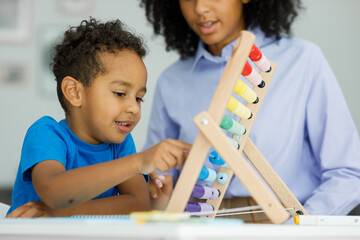 Teacher and little cute boy sitting at desk doing math using abacus doing homework early education