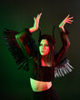 © faestock - portrait of beautiful asian model with dark hair, wearing black gothic skirt costume, angel feather wings with horned headdress. Posing with gestural hands  on dark silhouette  studio background.
