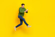 © deagreez - Photo of funky excited guy wear green sweater jumping writing modern device empty space isolated yellow color background