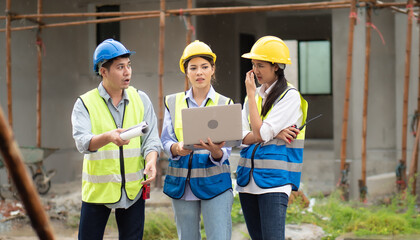 Female construction engineer holds computer laptop meeting with architect teamwork. Multiracial people group wear safety hardhat using laptop brainstorming on housing development at construction site