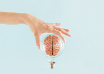 female hand holds transparent light bulb with human brain on isolated pastel blue background. minima