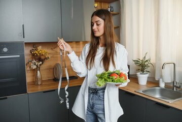 Wall Mural - Happy young woman preparing salad in kitchen. Healthy diet