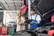 © bung - Pretty woman explain the problem of car to the professional vehicle maintenance man in uniform at garage. Car repair service concept. Customer feeling happy in auto service center.