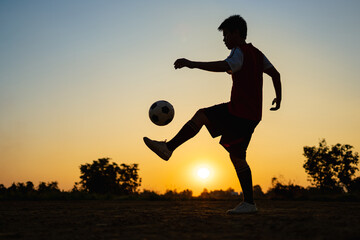 Silhouette action sport outdoors of kids having fun playing soccer football for exercise in community rural area under the twilight sunset sky. Picture with copy space.