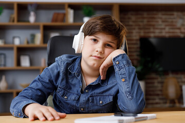 Young boy studying remotely at home using laptop. Tired schoolboy falling asleep during an online lesson with teacher. Distance learning is boring and uninteresting. Web cam view