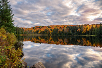 Wall Mural - Dramatic sunset sky over a lake wtih forested shores at the peark of autumn colours. Reflection in water.