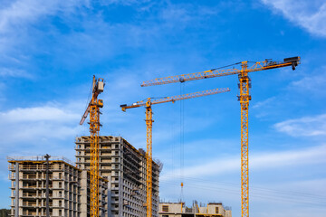 Construction site and yellow crane backdrop the blue sky. Yellow cranes build a multistory building in half of construction. Construction of a building