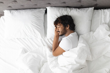 View above of eastern guy sleeping alone in bed