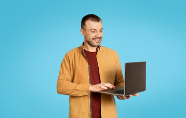 Poster - Successful Freelancer Male Using Laptop Computer Over Blue Studio Background