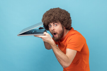 Wall Mural - side view of surprised man with afro hairstyle wearing orange t-shirt sees shocking information on s