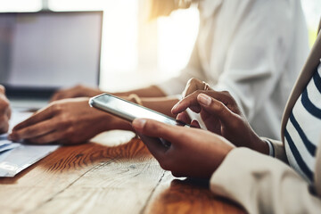 Closeup of a businesswoman hands on the phone texting colleagues, replying to messages or social media. Marketing professional female taking a break from working together with her team on a project