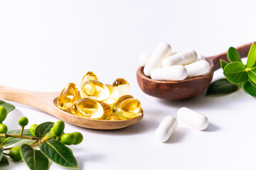 Wall Mural - Natural herbal medicine concept. Two wooden spoons with natural medical capsules for healthy lifestyle and immunity support and fresh green leaves on white background close up.