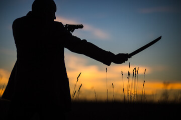 Silhouette of a demon and vampire hunter with a dramatic sky in the background. A man with a katana and a revolver. Fantasy and halloween concept