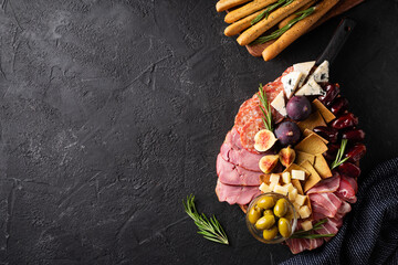 Meat, cheese and snackes plate, board and grissini on black background