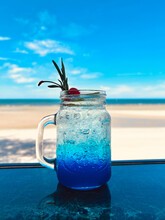 Summer Holiday Concept.  Blue Hawaii Soda Cocktail On Marble Table With Blur White Beach And Blue Sky Background.