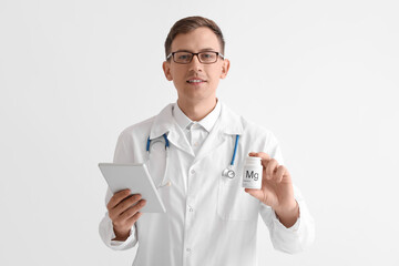 Wall Mural - Young doctor with tablet computer and bottle of magnesium pills on white background