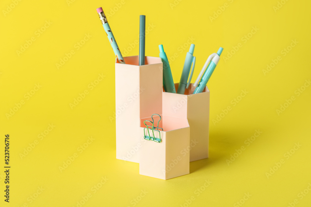 Pen cups with stationery on yellow background