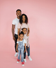 Wall Mural - Cheerful african american family of four, standing one behind other and smiling at camera on pink background, banner, free space.