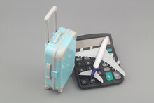 Travel Budget And Airplane Tickets Price Concept. Airplane On Calculator And Suitcase On Gray Background.