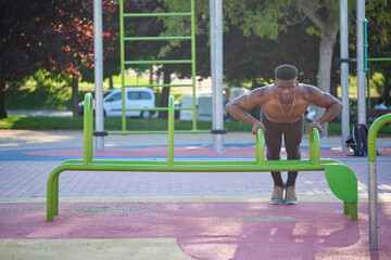 Wall Mural - Young fit shirtless black man doing push-ups on parallel bars in a calisthenics park outdoors on sunny day. Fitness and sport lifestyle.