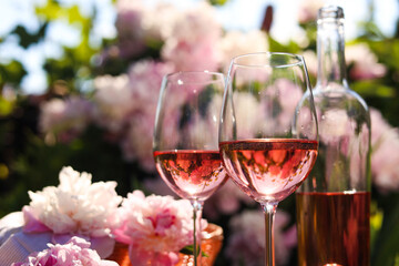 Canvas Print - Bottle and glasses of rose wine near beautiful peonies in garden, closeup. Space for text