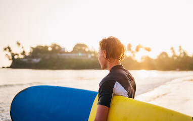 Wall Mural - Young teenager boy with colorful surfboard go to the sea for surfing. He enjoying a beautiful sunset light on Dewata beach on Sri Lanka. Active sport vacation and exotic countries traveling concept.