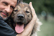A middle-aged man hugs a dog on a walk. Close-up.