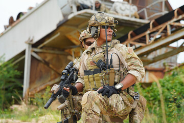 2 Army military soldier in the battle field sitting knee down on the ground hold the gun alert look around ready to fire weapon 
