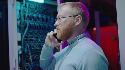Chest up shot of professional IT engineer speaking on mobile phone while working in server room of data center