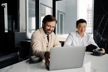 Two business people sitting by table with laptop and cups