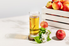 Apple Juice. Full Glass Of Natural Apple Juice On A Wooden Podium With Red Apples And Blossom Branche On A White Table With Copy Space. Summer Natural Drink. Soft Focus Stile