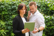 © serhii - business partners man and woman are discussing something using smartphone tablet laptop. a team of two professional people discusses, decides, consults against the backdrop of green plants.