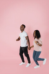 Wall Mural - Full length shot of a african american man and woman in casual outfit walking or running together isolated on pink background.