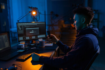 Poster - cybercrime, hacking and technology concept - male hacker with smartphone using computer virus program for cyber attack in dark room