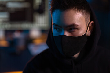 Poster - cybercrime, hacking and technology concept - close up of hacker wearing black mask and hoodie in dark room with computers at night