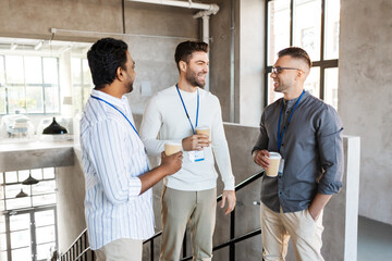 Poster - business, people and corporate concept - happy smiling businessmen or male colleagues with name tags drinking takeaway coffee at office