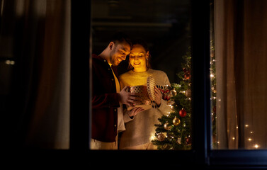 Poster - holidays, celebration and people concept - happy couple opening christmas gift box with magical light inside at home